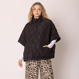 Woman wearing a black patterned poncho over a white shirt and leopard print pants on a beige background