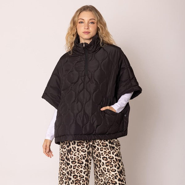 Woman wearing a black patterned poncho over a white shirt and leopard print pants on a beige background