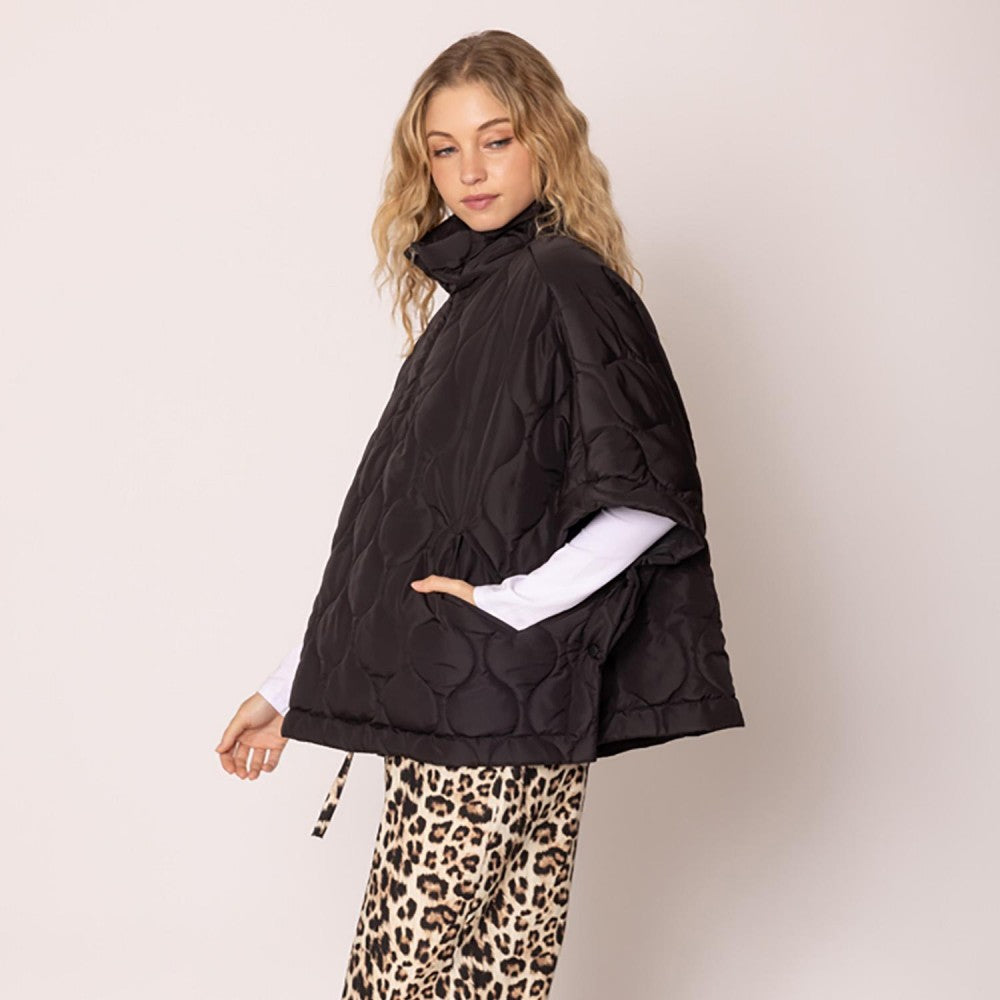 Woman wearing a black quilted poncho over leopard print pants on a beige background