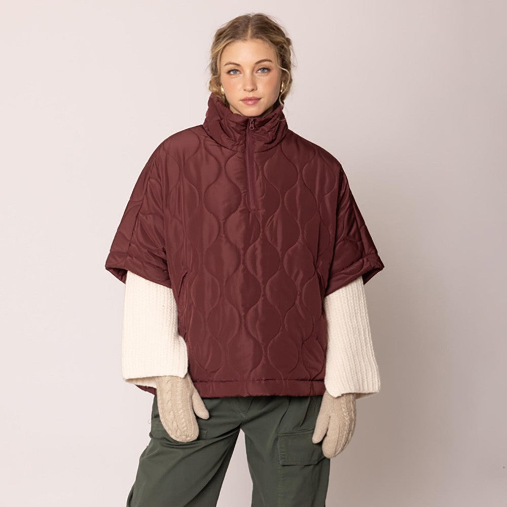 Woman wearing a maroon quilted poncho over a white shirt with a beige background