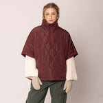 Woman wearing a maroon quilted poncho over a white shirt with a beige background
