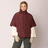 Woman wearing a maroon quilted poncho over a white shirt with a beige background