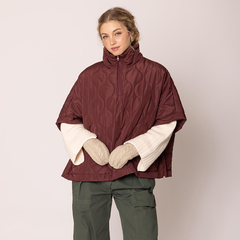 Woman wearing a burgundy patterned jacket, green pants, and white gloves on a plain background
