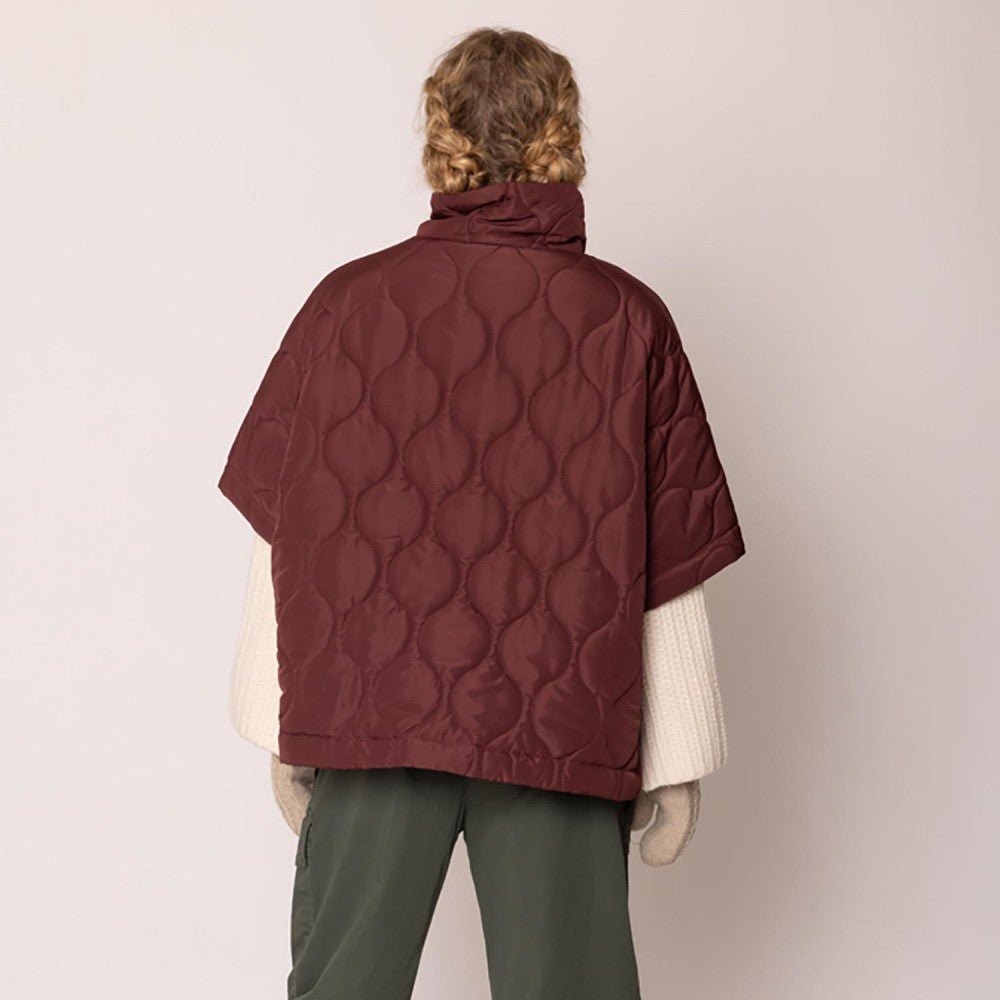 Person wearing a quilted burgundy jacket on a plain background
