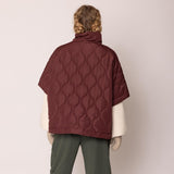 Person wearing a quilted burgundy jacket on a plain background