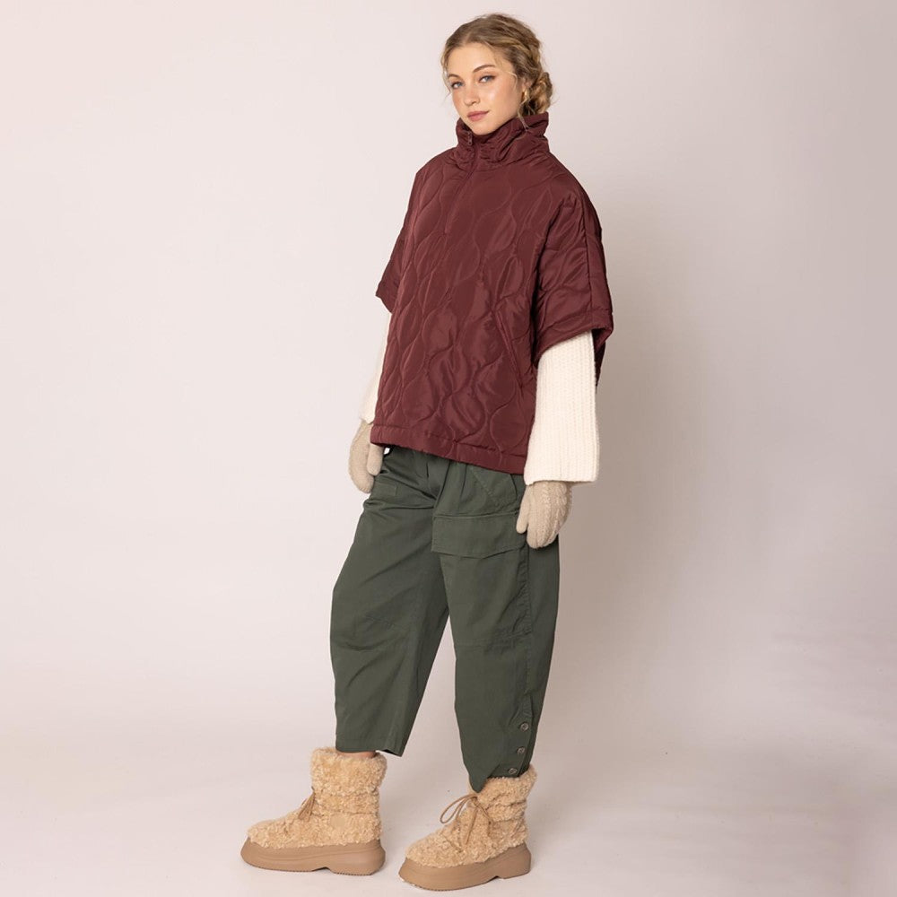 Person wearing a burgundy quilted jacket, green pants, and beige boots on a plain background