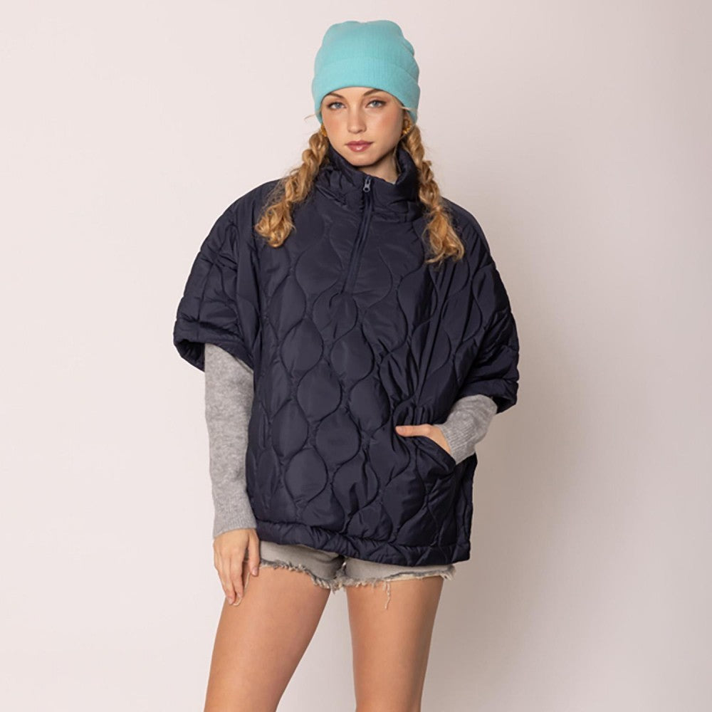 Person wearing a navy blue quilted jacket and light blue beanie on a plain background