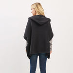 Woman wearing a dark gray hooded poncho on a light gray background