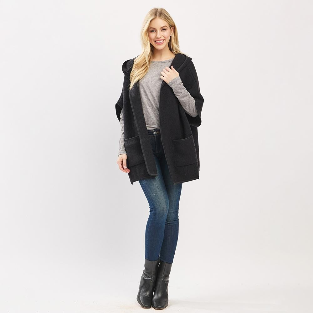 Woman wearing a black cardigan, gray sweater, blue jeans, and black boots on a white background