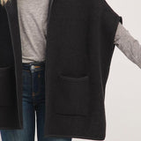 Person wearing a black vest over a gray shirt and blue jeans on a light gray background