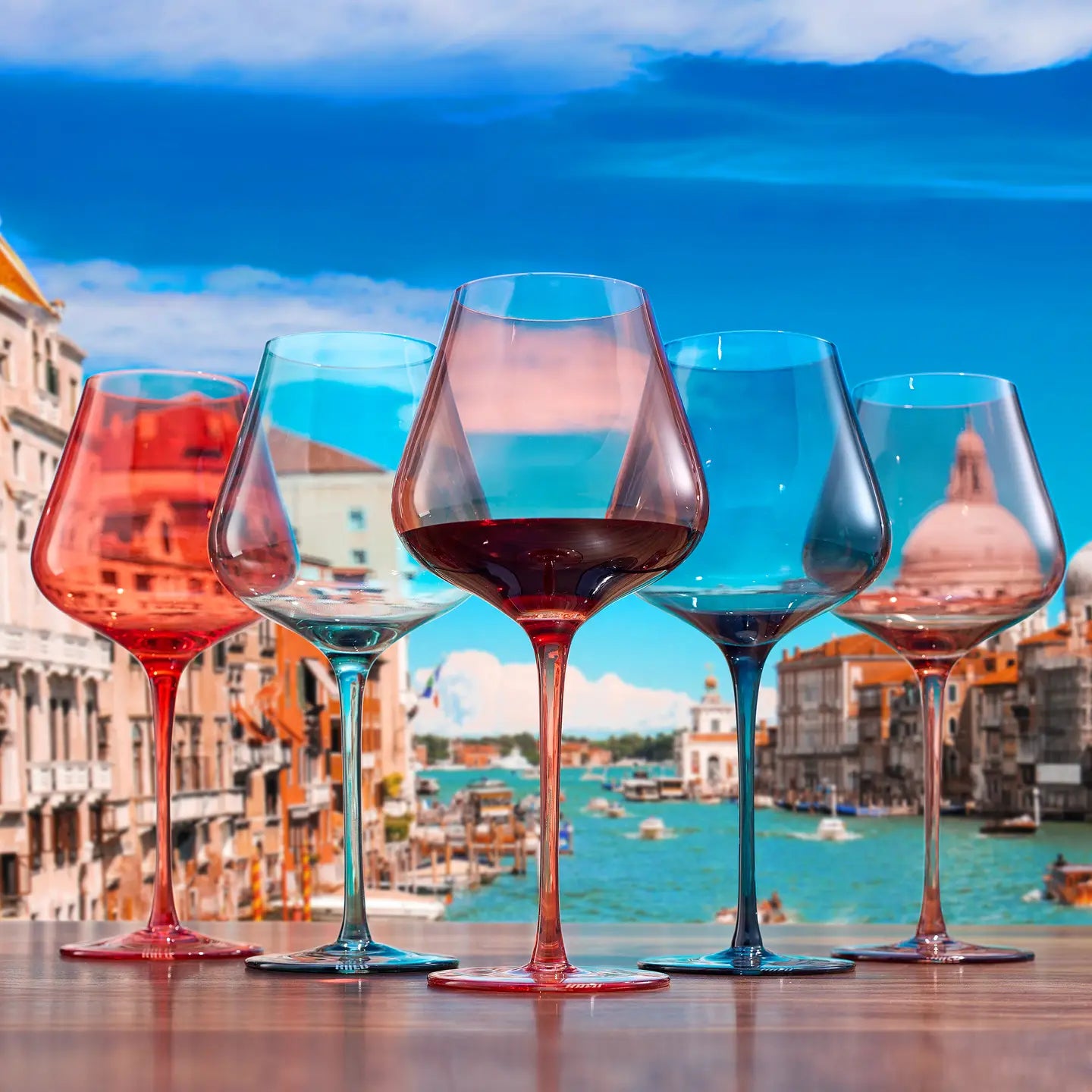 Five wine glasses with colored stems in front of a scenic cityscape