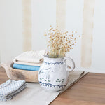 Ceramic vase with dried plants on a wooden surface with folded cloths