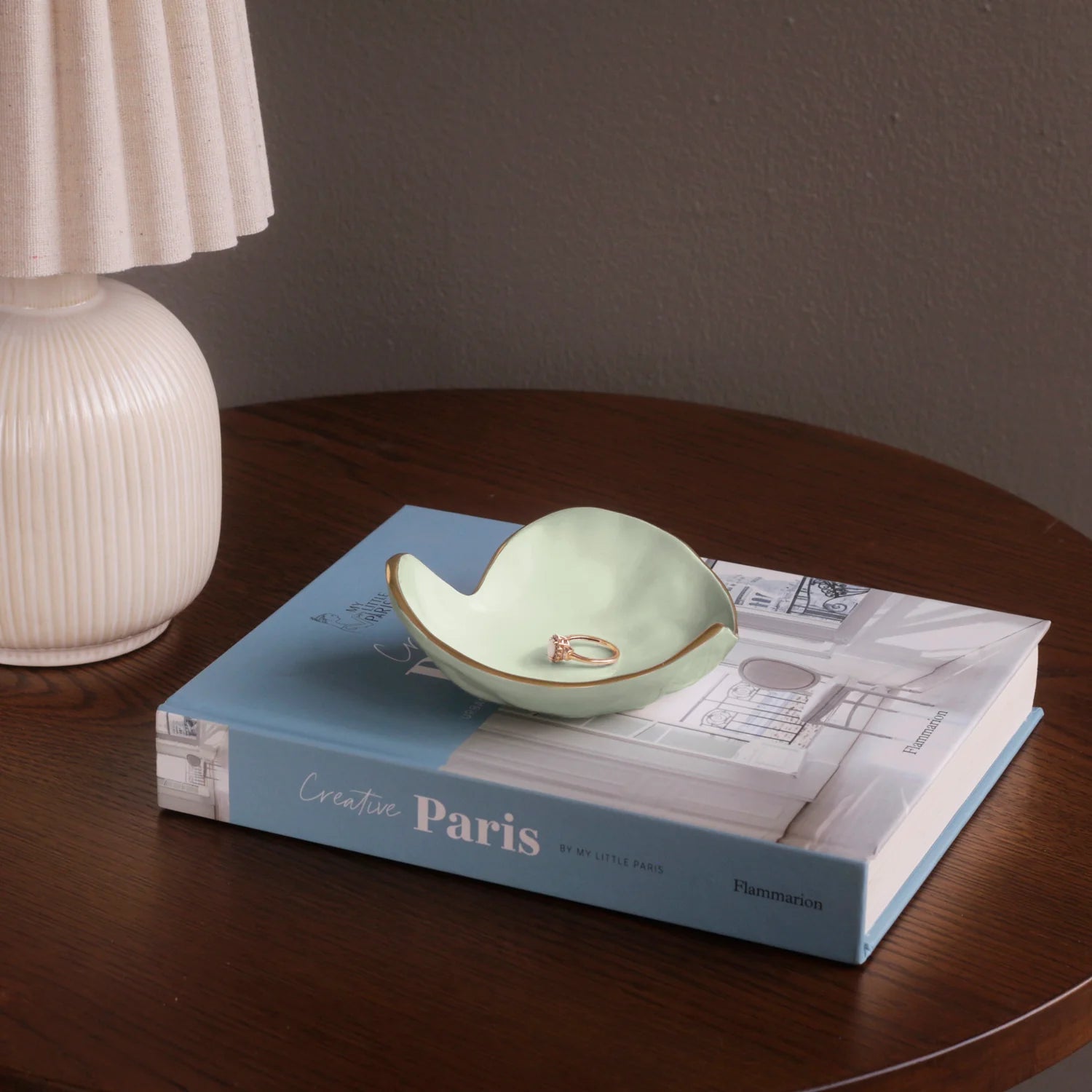 Green ceramic dish on a book with a ring inside, on a wooden table.