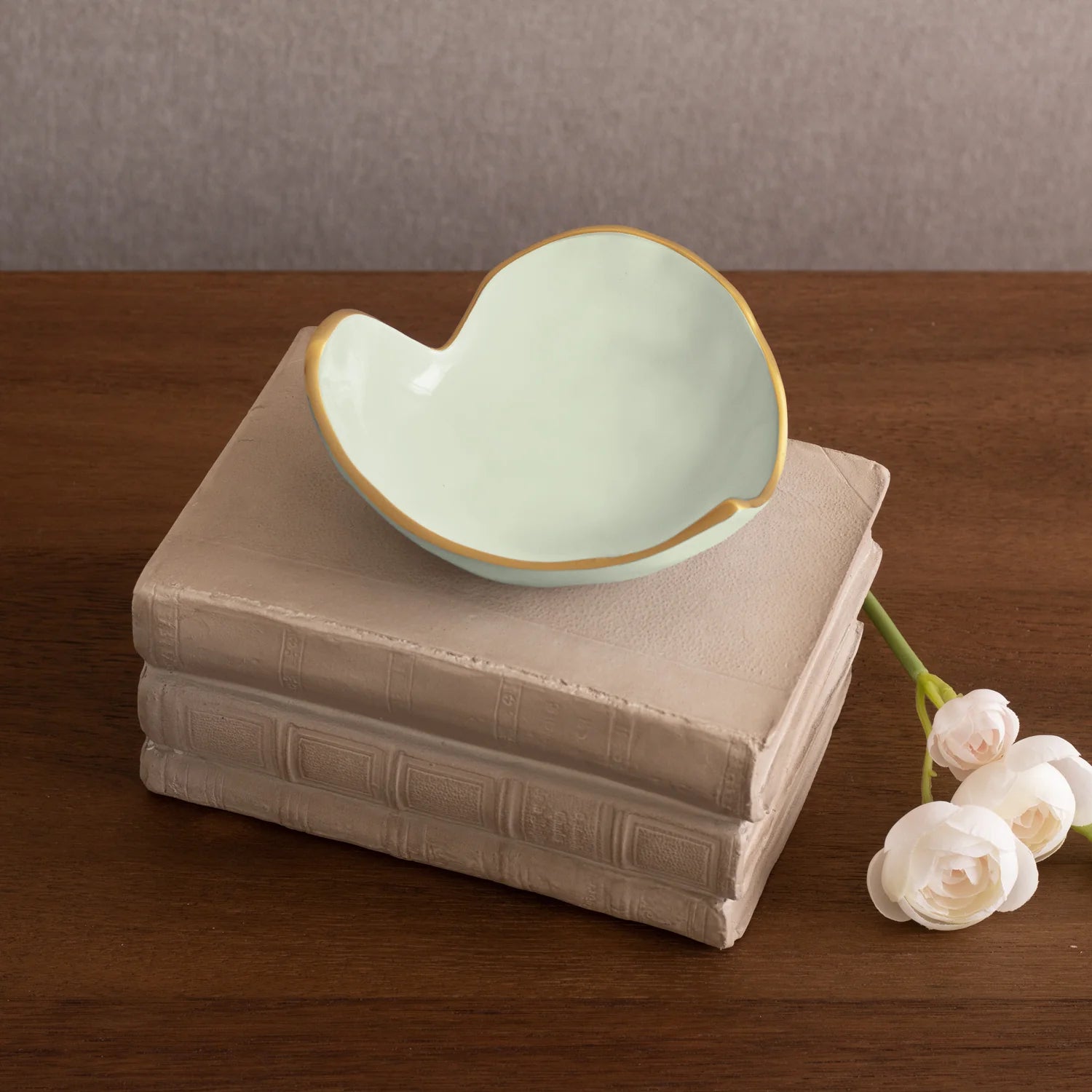 Heart-shaped ceramic bowl on a stack of books with white flowers on a wooden surface