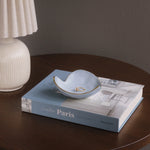 Small blue dish with gold interior on a book titled 'Creative Paris' on a wooden surface.