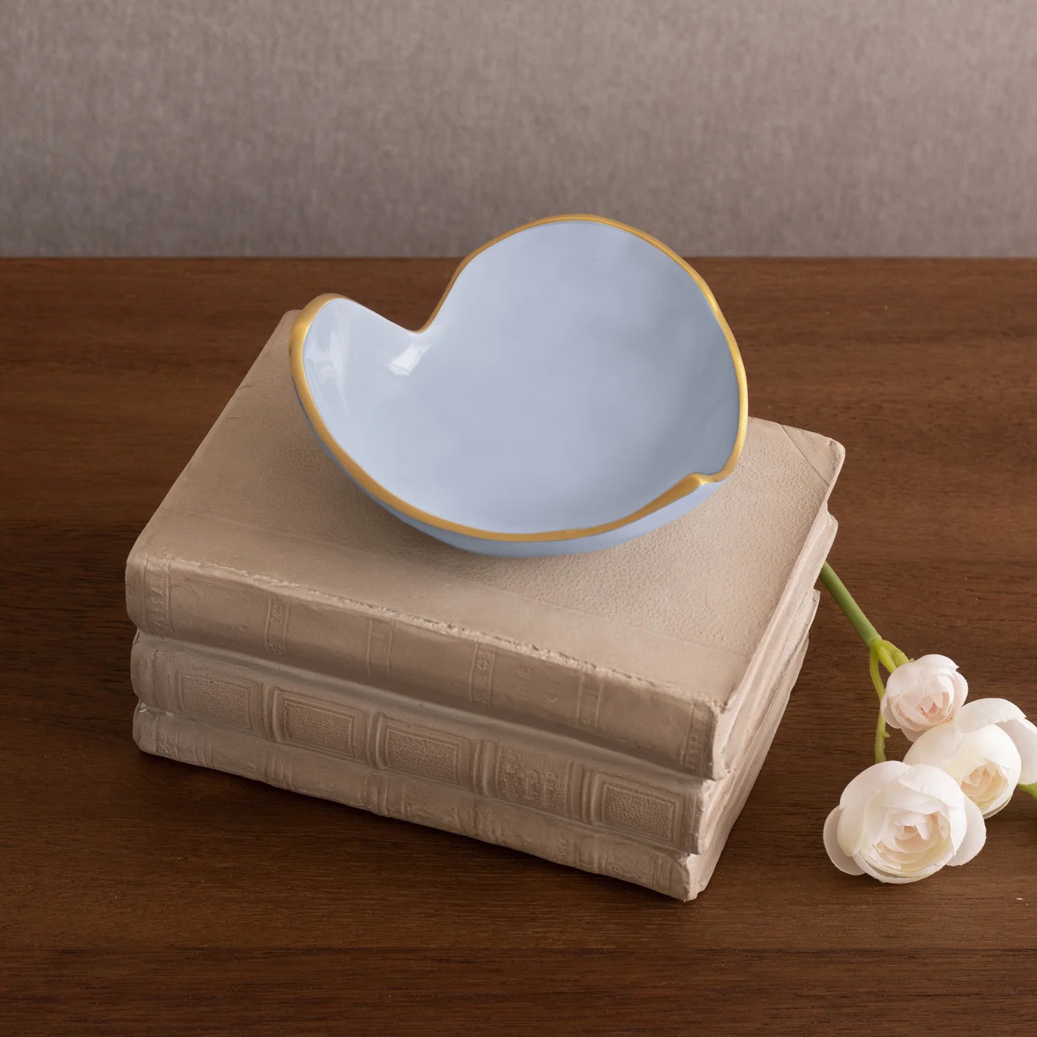 Blue ceramic bowl on a stack of books with white flowers on a wooden surface