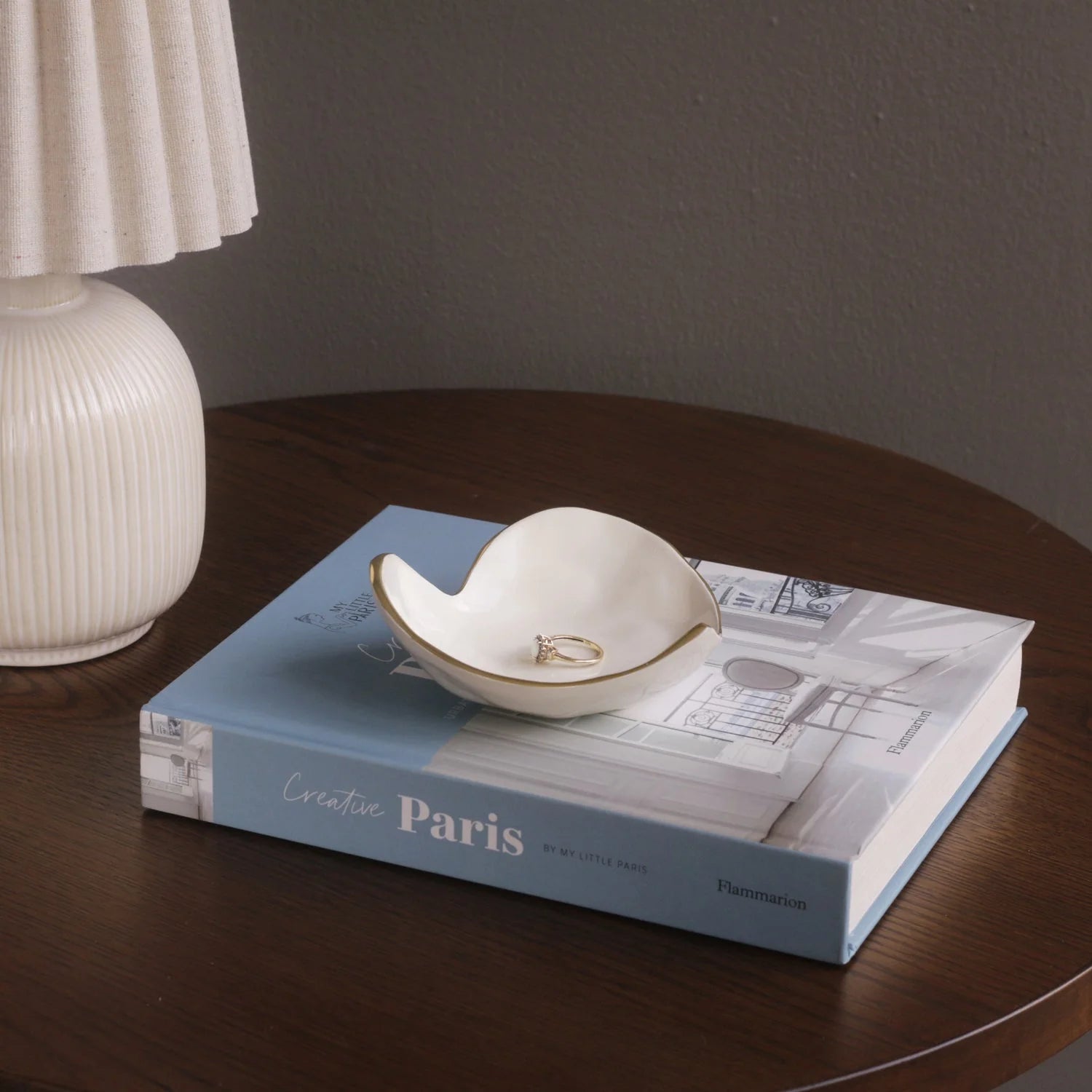 Small white dish with rings on a book titled 'Creative Paris' on a wooden table.