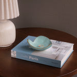 Teal ceramic dish with gold interior on a book titled 'Creative Paris' on a wooden table.
