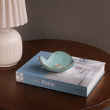 Teal ceramic dish with gold interior on a book titled 'Creative Paris' on a wooden table.