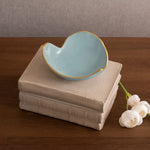 Heart-shaped blue ceramic dish on stacked books with white flowers on a wooden surface