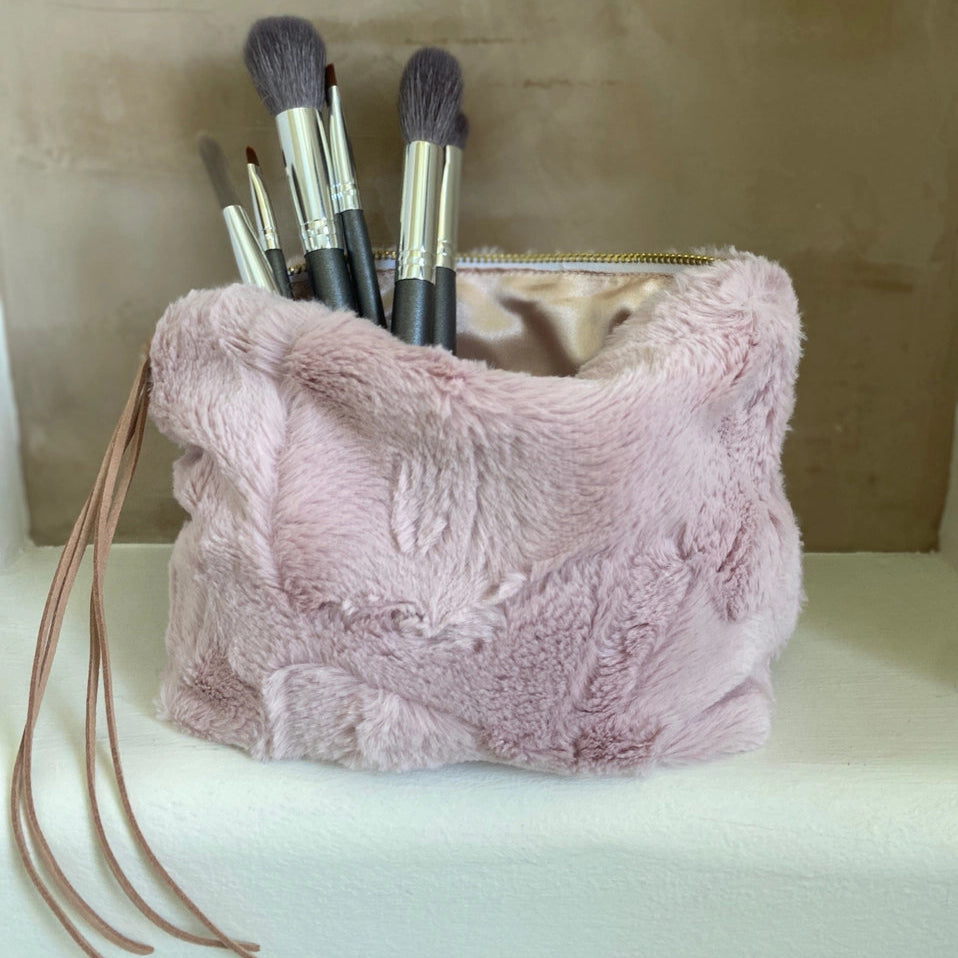 Pink fluffy makeup bag with brushes on a neutral background