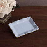 encanto vento small rectangular tray periwinkle on a wooden surface with a vase of flowers.