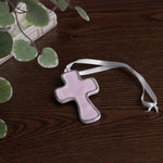 encanto athens cross ornament lilac with a white ribbon on a wooden surface with green leaves.