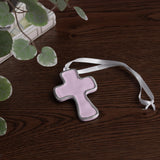 encanto athens cross ornament lilac with a white ribbon on a wooden surface with green leaves.