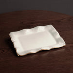 Rectangular white ceramic plate with gold rim on a dark wooden surface