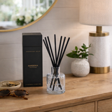Aromatherapy diffuser with black sticks on a wooden surface next to a box and lamp.