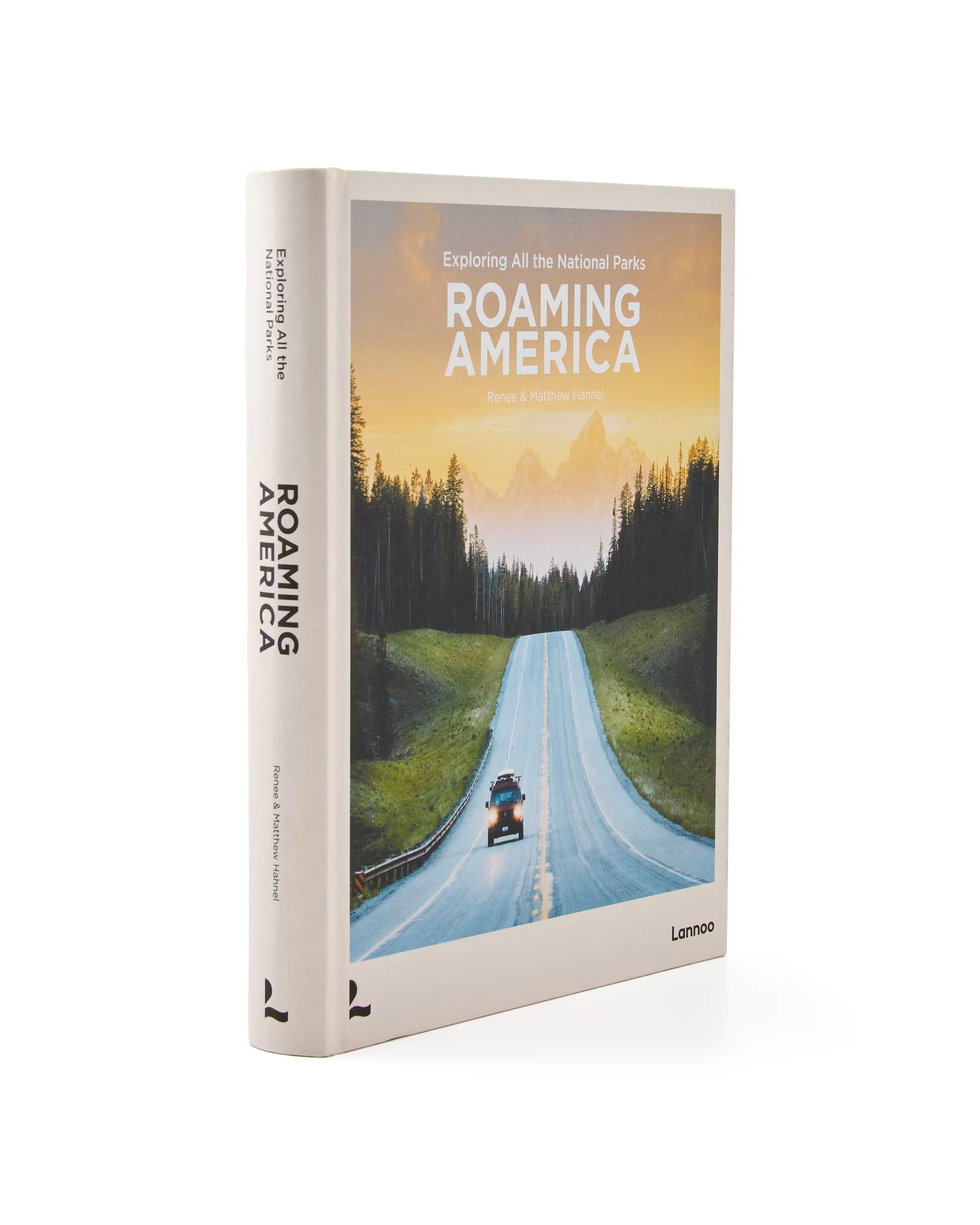 A hardcover book titled 'Roaming America: Exploring All the National Parks' standing upright on a white background. The cover features a scenic photograph of a winding road through a forest under a warm sunset sky, with the title in bold white text.