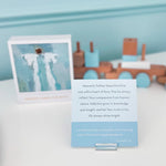 Card with text and an angel illustration next to toy train and car on a light blue background