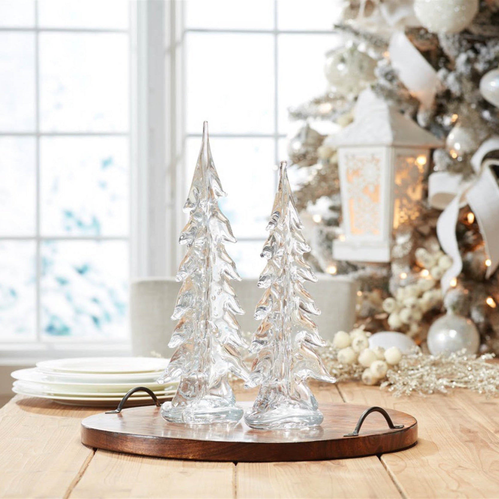 Decorative glass Christmas trees on a wooden table with a Christmas tree in the background.