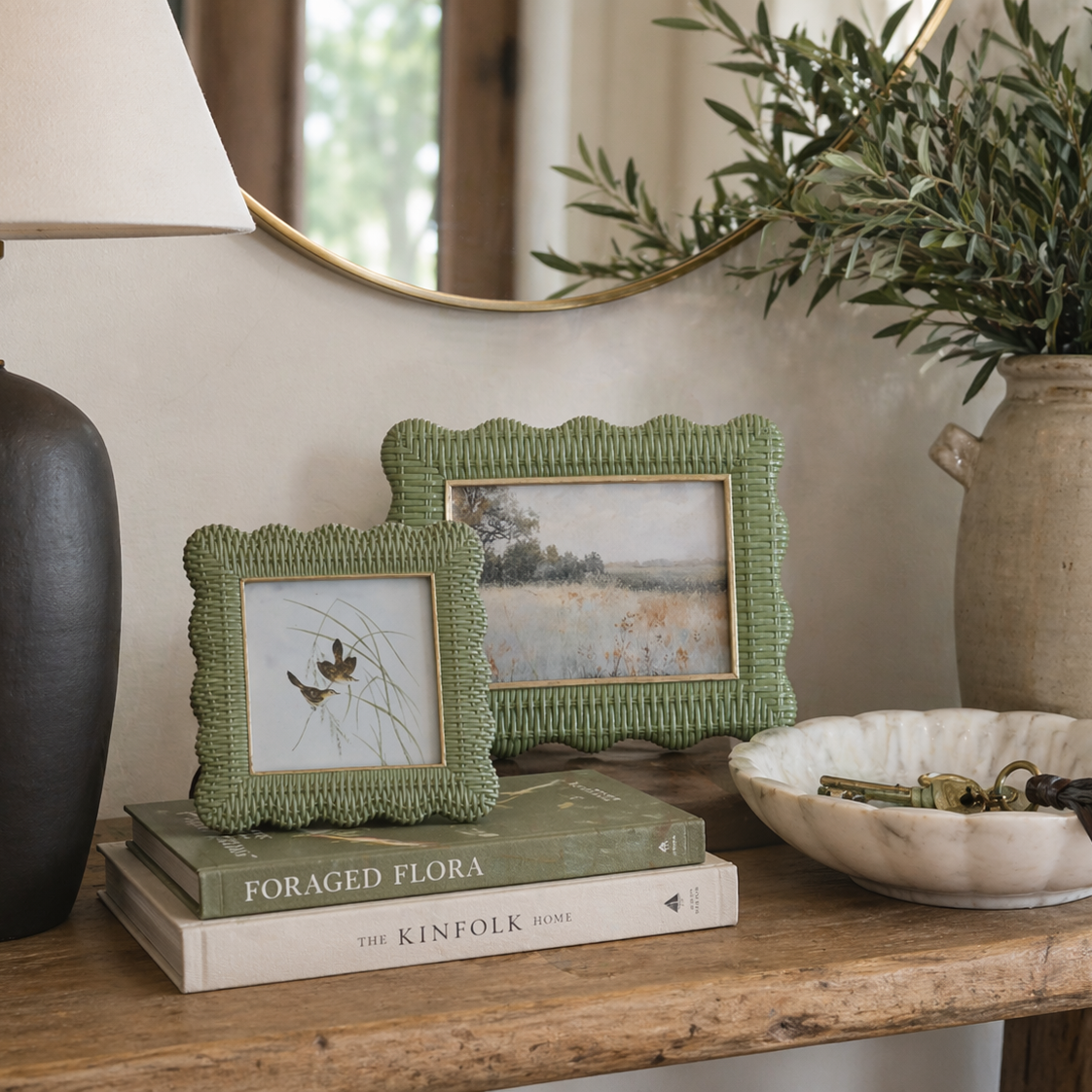 Decorative setup with framed pictures, books, a vase, and a plant on a wooden surface.