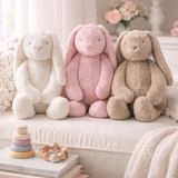 Three plush bunny toys in white, pink, and beige sitting on a surface with soft focus background.