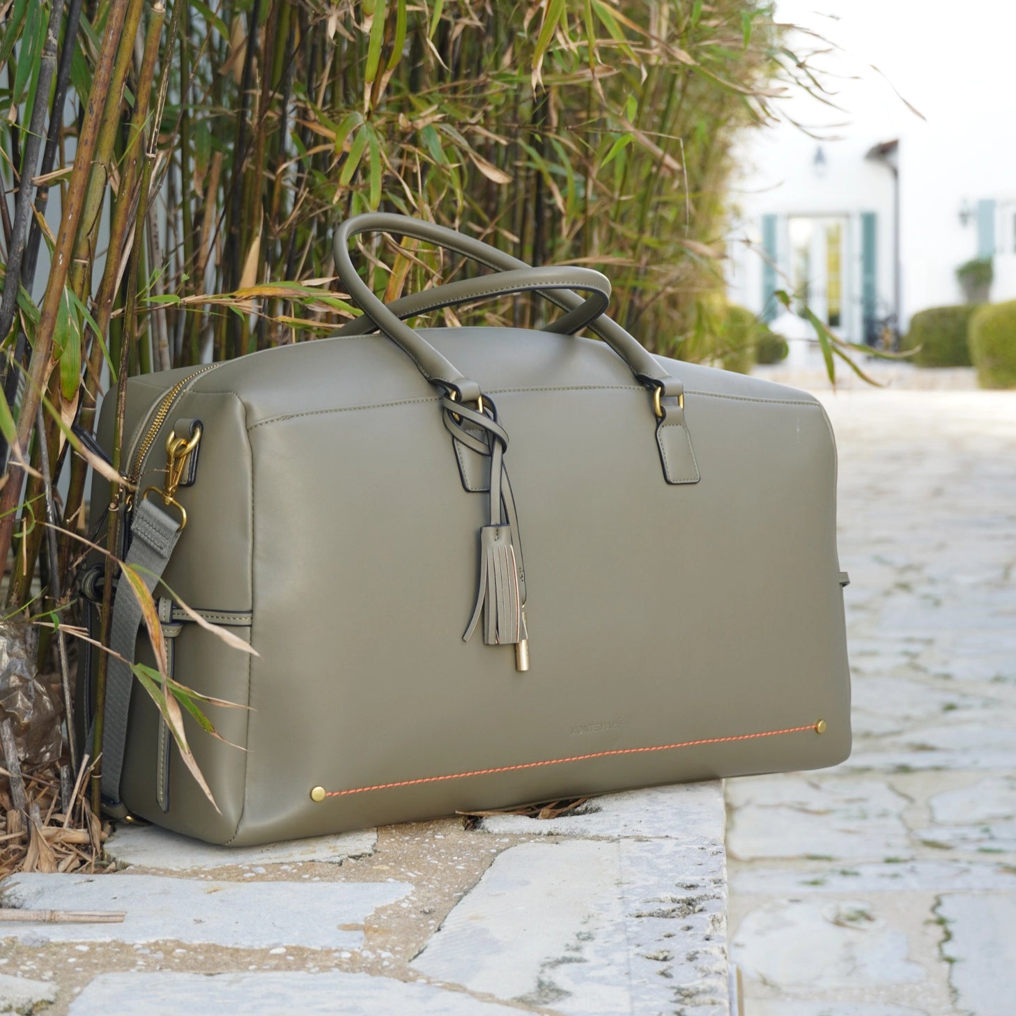 Montemare Roma Duffle in Olive on a stone path with bamboo plants in the background