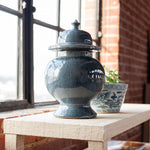 dark gray ceramic jar with a lid on a wooden surface near a window