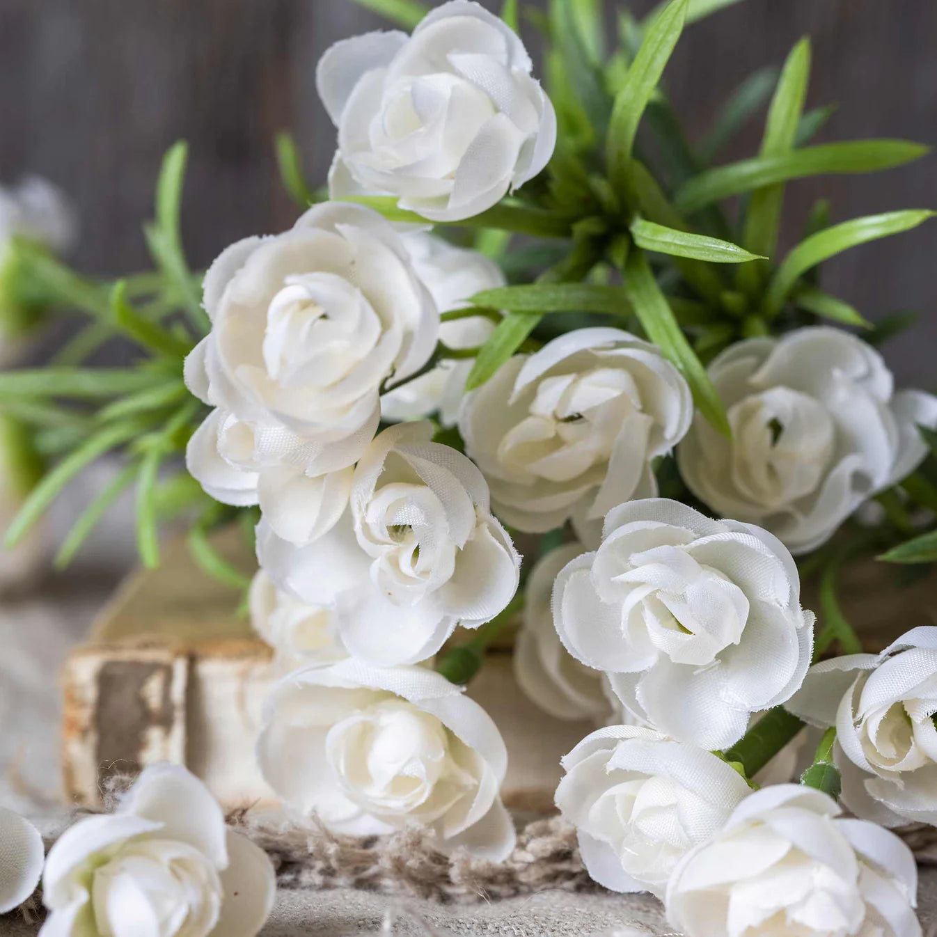 Bouquet of white artificial roses with green leaves on a textured surface.