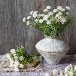 White flowers in a textured vase on a wooden surface