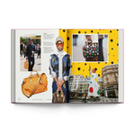 An open book spread featuring Louis Vuitton imagery, including a large orange monogram shoulder bag, a model in a blue patterned jacket holding a Louis Vuitton bag, a smaller multicolor polka-dot handbag, and a collage layout on a white background.