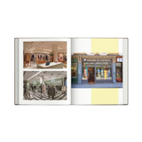 An open book showing two fashion retail interior and storefront photographs on the left and right pages, with pale yellow graphic blocks on the right page, photographed against a light gray background.