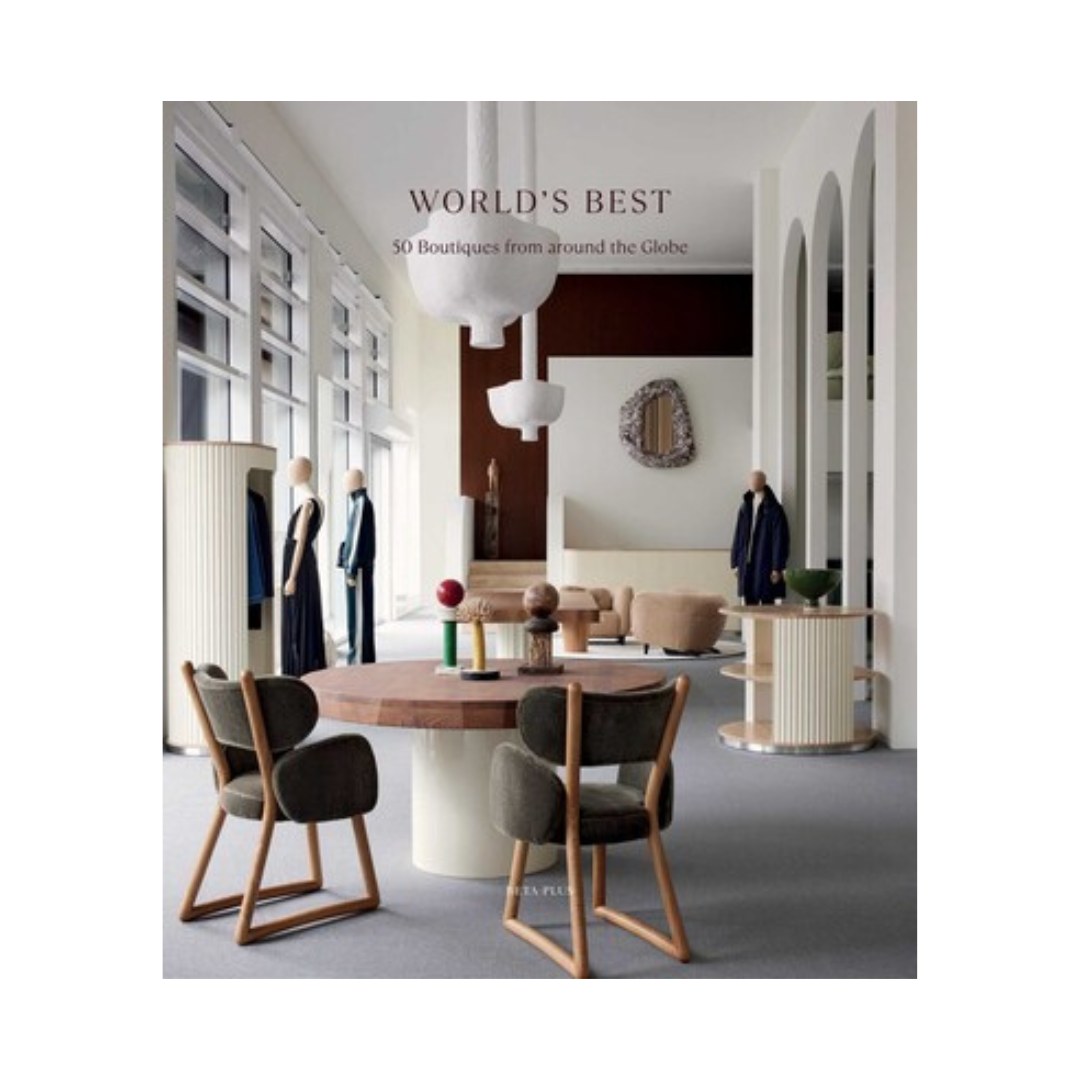 A book cover titled 'WORLD'S BEST 50 Boutiques from around the Globe' featuring a photograph of a modern, stylish boutique interior with wooden chairs, a round table, and mannequins displaying clothing.