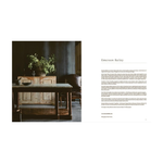 An open book view of interior design spread with a dark, moody room scene on the left showing a rustic wooden sideboard and table with plants, and a text column on the right headed Emerson Bailey.