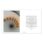 An open book spread showing a large architectural photograph of a spiral staircase on the left page and a column of text on the right page, photographed against a white background from the hardcover book "contemporary living yearkbook 2026" on a white background