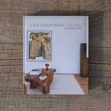 A hardcover book titled 'Contemporary Living Yearbook 2026' by Ben Plain, featuring a modern living room interior cover design, photographed flat on a rustic wooden surface.