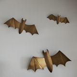 three gold winged bats in varying sizes hanging on a wall
