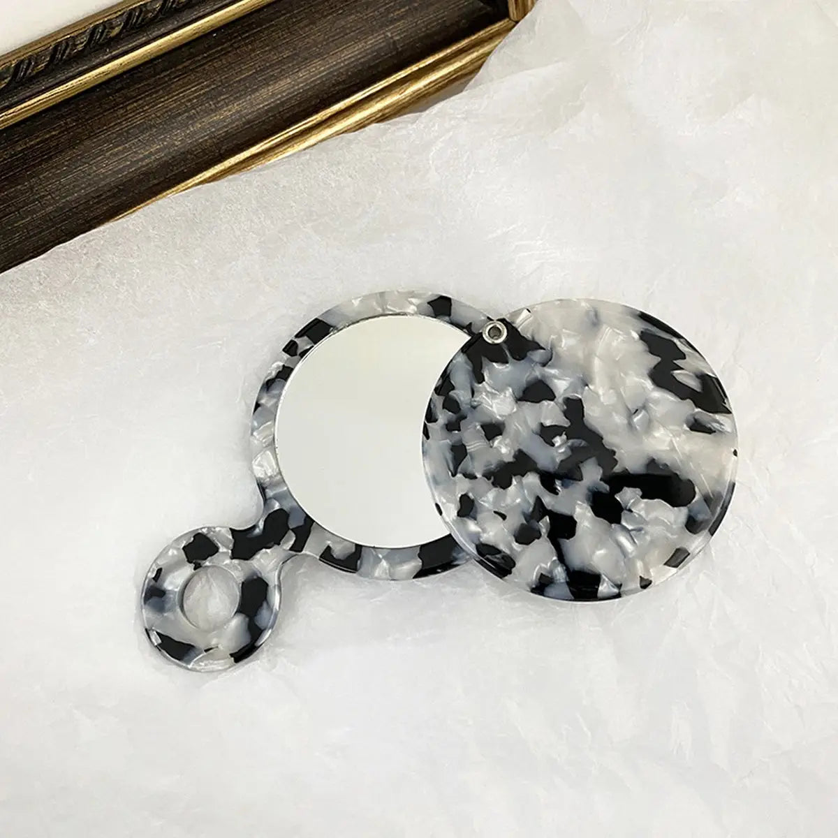 Black and white marbled circular mirror on a white surface with a wooden frame in the background.