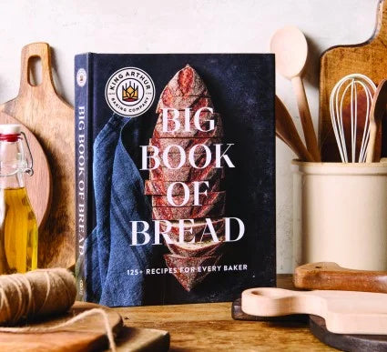 Cookbook titled 'Big Book of Bread' on a kitchen counter with baking utensils.