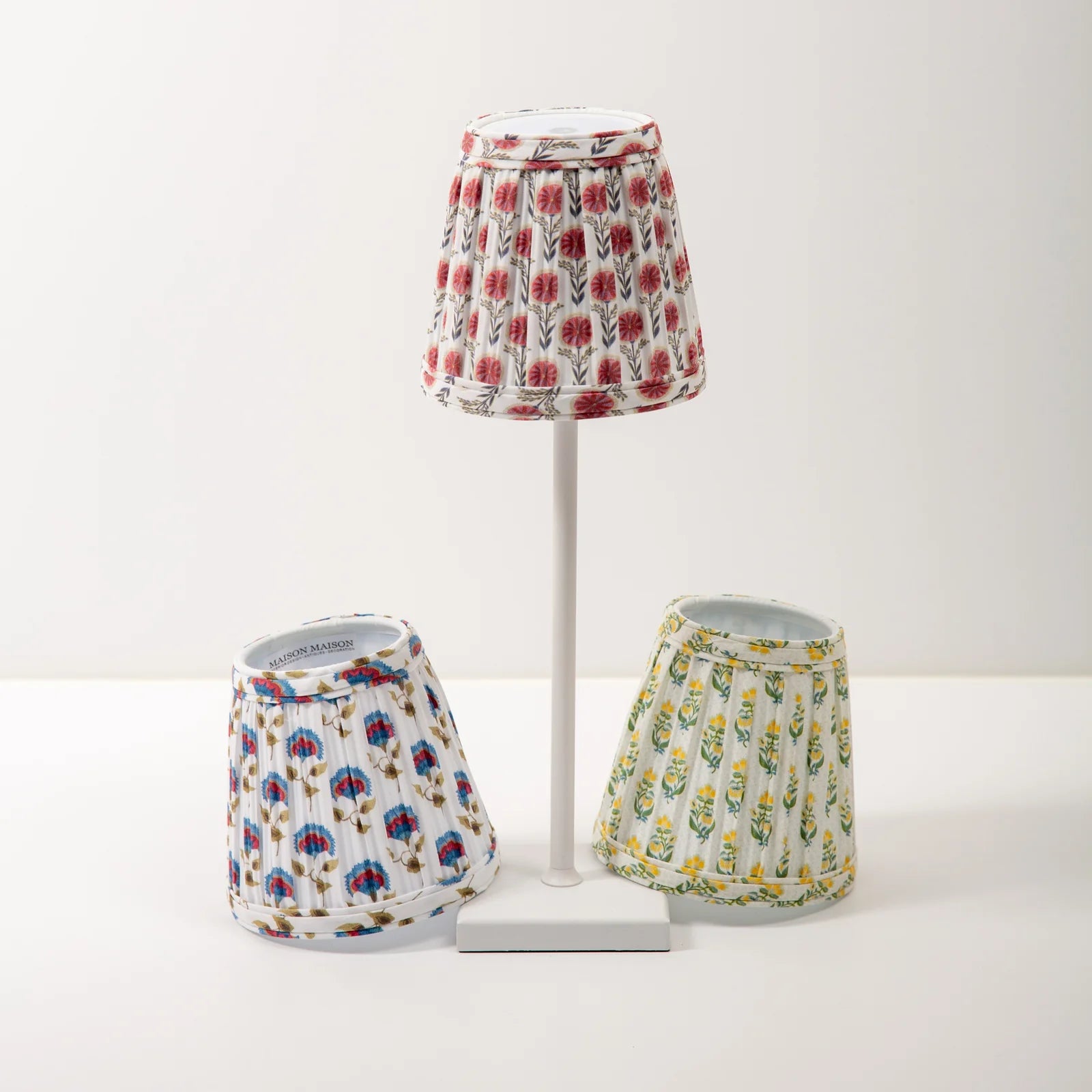 Set of three floral-patterned lampshades on a white stand against a white background