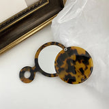 Tortoiseshell round compact mirror on a white surface with a gold frame in the background.